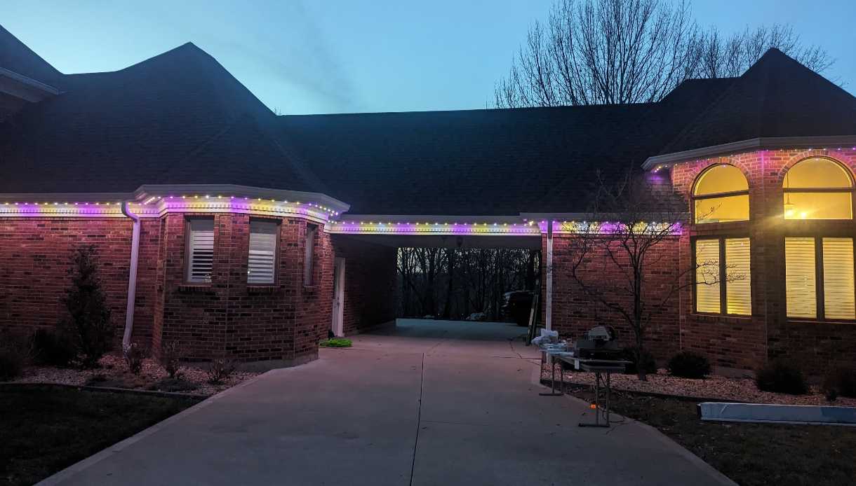 Actual Bright Home installation with purple, yellow, and white lighting along a brick home at dusk